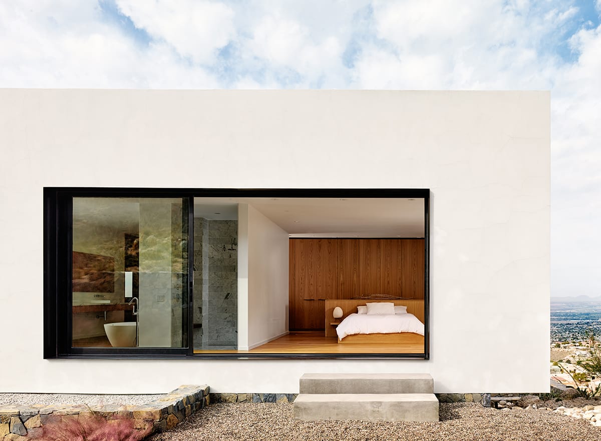 The master suite's multi-slide door seamlessly merges the interior of the upper volume with the rugged landscape outside.