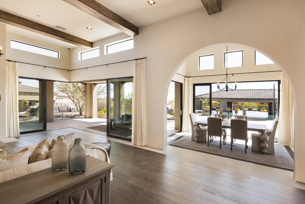 An indoor living and dining room is blended with the outdoors by surrounding moving walls of glass.