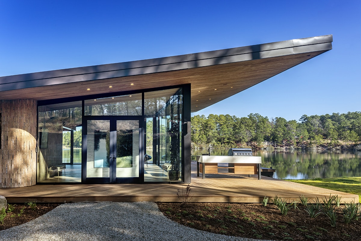 A front entrance, with deck and outdoor kitchen beside it overlook a lake.