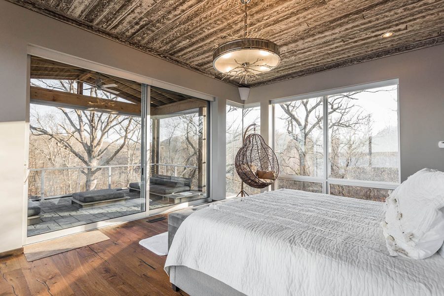 A rustic bedroom with a reclaimed wood ceiling has a large aluminum sliding glass door leading to a private covered patio.
