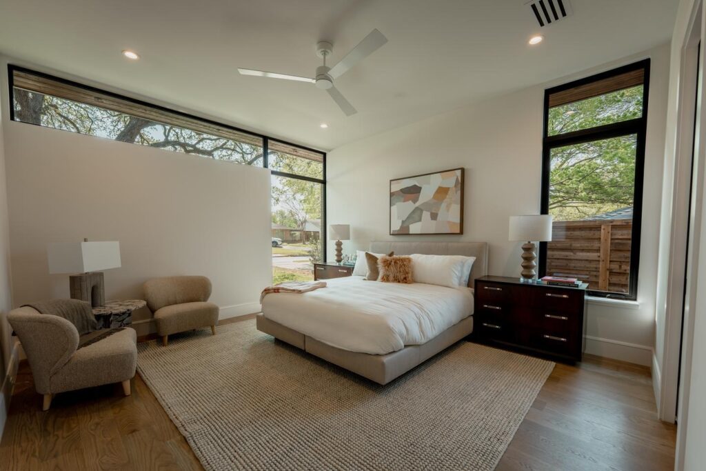 A spacious bedroom includes multiple windows in unique configurations, which let in natural light and contribute to the modern aesthetic of the room.