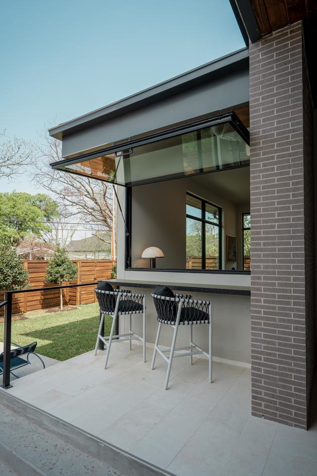 A home features a patio area with two barstools facing an open window that is hinged at the top and provides access to an interior living space.