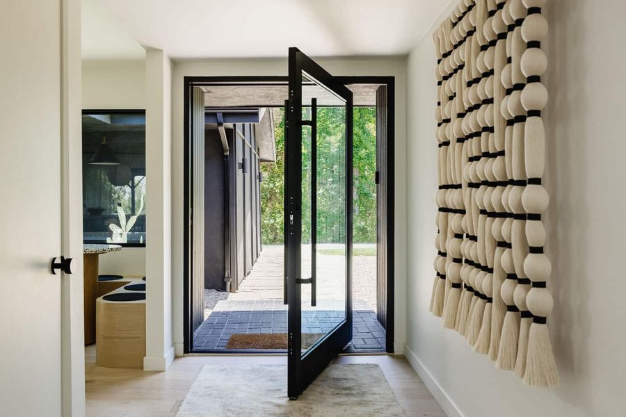 A view of an open black pivot entry door in a modern home, looking out to greenery.