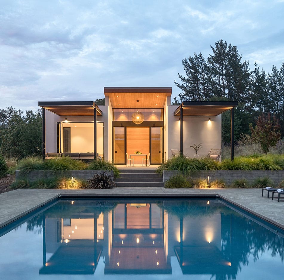 A front view of the guest house during dusk with the pool in the foreground.