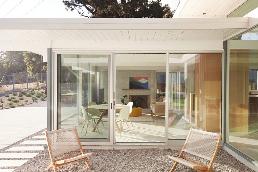 A mid-century modern home features a glass wall with a sliding glass door.