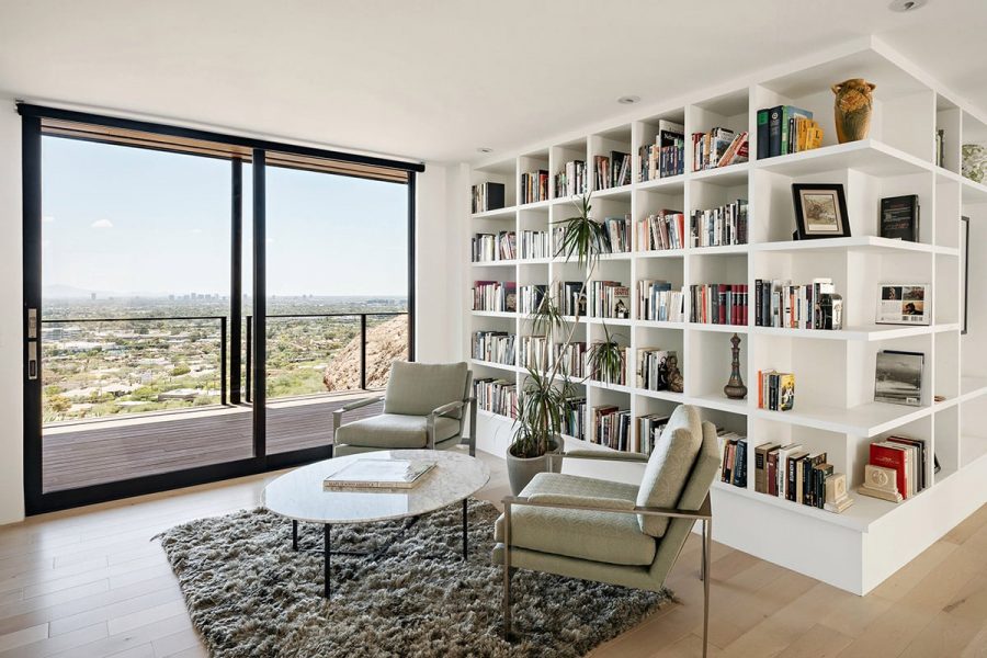 RR-1577-web A modern library has white shelves with a tall sliding glass door leading to balcony and view of the desert.