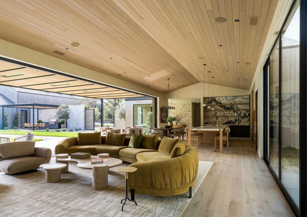 A living room with a modern gold sofa opens onto a patio with a large opening between them where a wall would be.