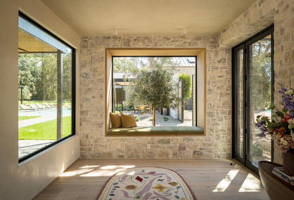 A light-filled foyer has two large fixed windows and a hinged door, one of the windows has a seat built into it.