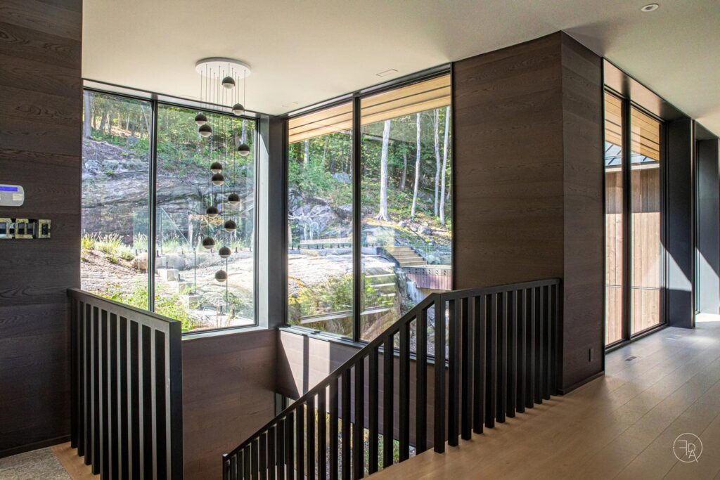 Looking out 90-degree corner windows at the top of a staircase, landscaping and natural bedrock can be seen in front of the tree line.