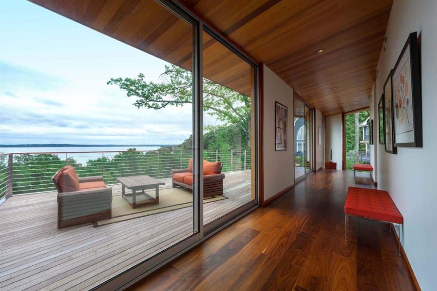 Two large sliding glass doors lead from a wood-floored hallway to a balcony deck overlooking a lake.